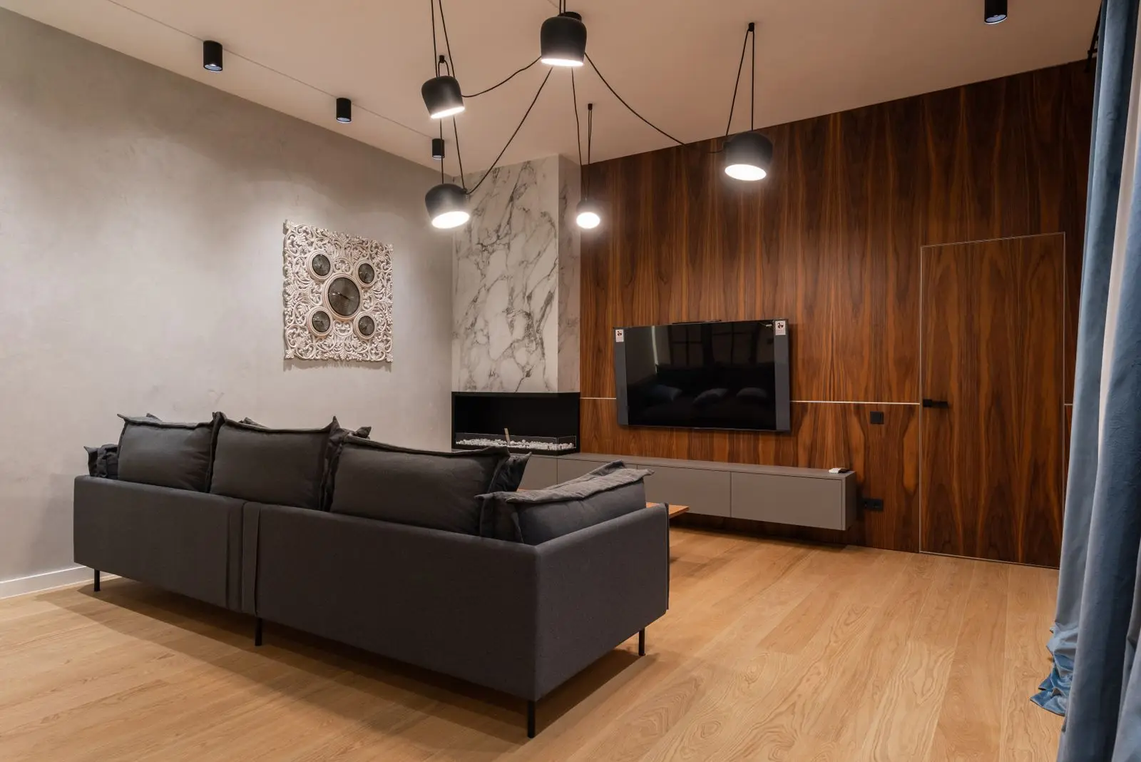 Szara sofa i wisząca szafka pod telewizorem na ścianie wykończonej drewnem
